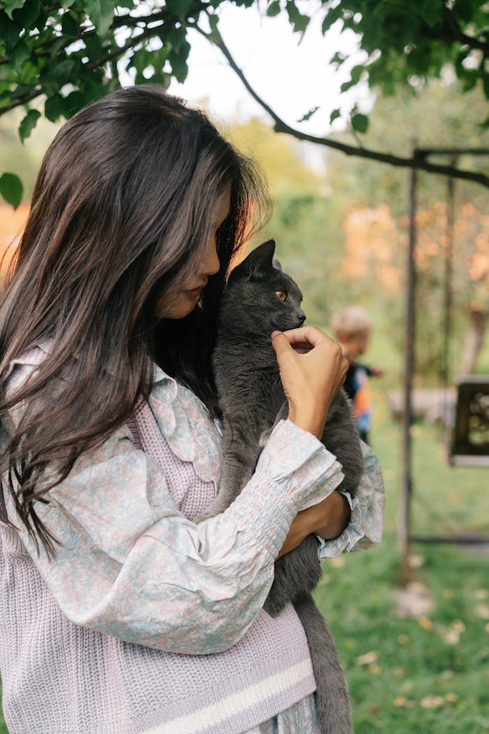 Charming scene of a young woman holding her cuddly gray cat outdoors.